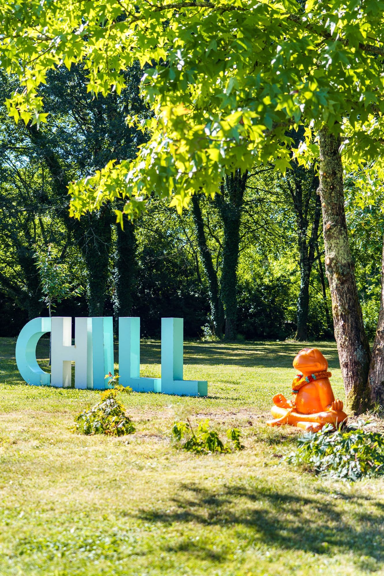 Les lettres CHILL dans l'herbe, un compagnon en peluche posé au pied d'un arbre