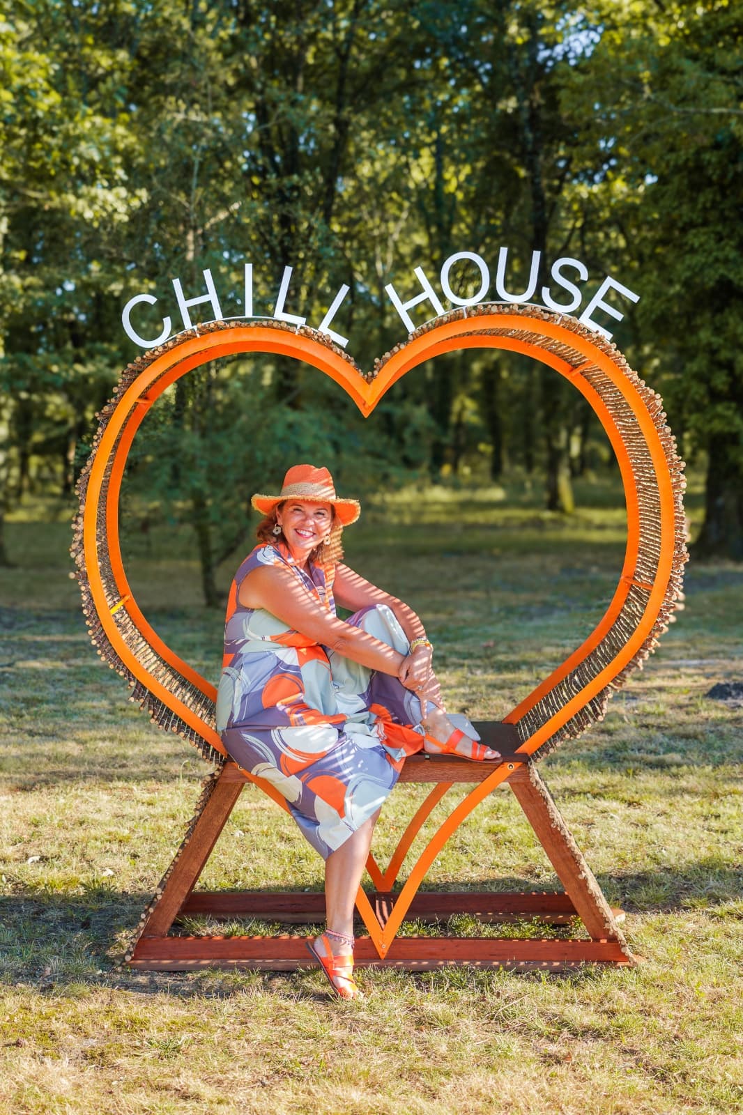 Emily, assise dans le grand cœur en bois « Chill House » installé dans le parc, chapeau de paille et sourire au soleil