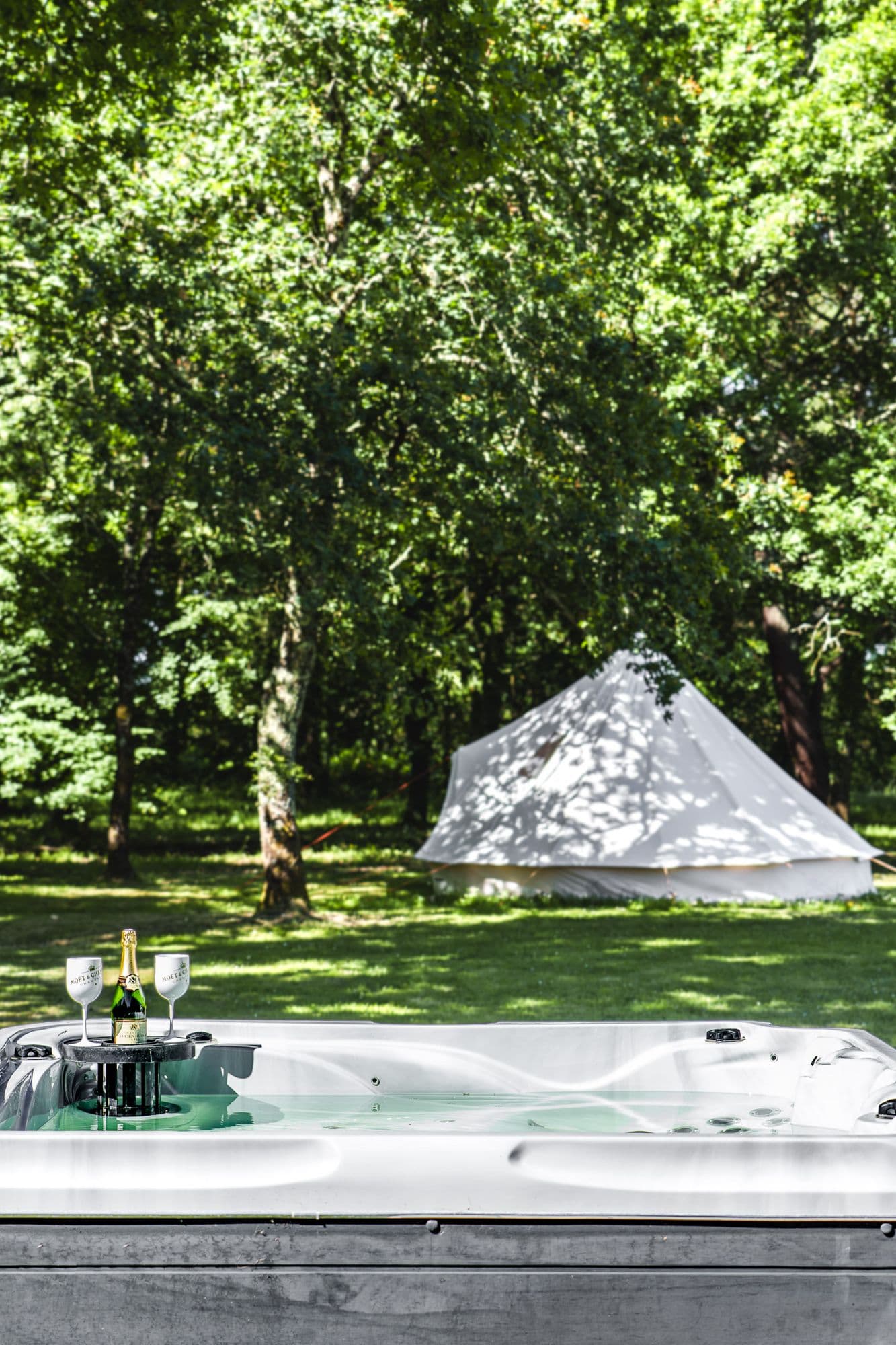 Le spa fumant, champagne servi, le tipi blanc dans le parc en arrière-plan